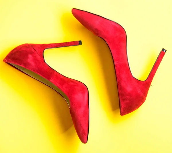 Footwear with thin high heels, stiletto shoes, top view. Shoes made out of red suede on yellow background. Pair of fashionable high heeled pump shoes. Feminine shoes concept