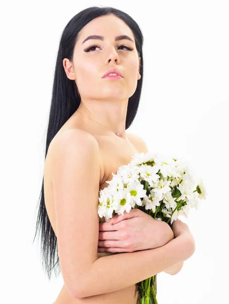 Κυρία καλύπτει τα στήθη με λουλούδια, απομονωμένα σε λευκό. Γυναίκα με ομαλή υγιές δέρμα φαίνεται ελκυστικό. Δέρμα υγεία έννοια. Κορίτσι στο ήρεμο πρόσωπό στέκεται γυμνή και κρατά τα άνθη χαμομηλιού μπροστά στο στήθος — Φωτογραφία Αρχείου