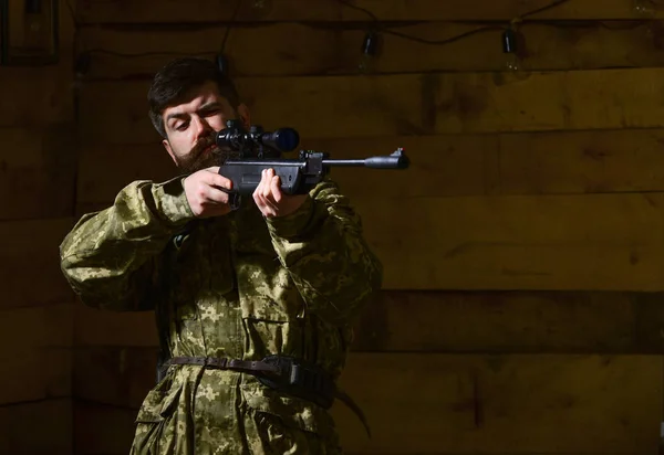 Człowiek z brodą nosi odzieży kamuflaż, drewniane wnętrze tła. Macho na ścisłe twarz w domu myśliwska. Hunter, brutalne hipster z pistolet cel przed polowaniem, miejsce. Koncepcja Huntsman — Zdjęcie stockowe