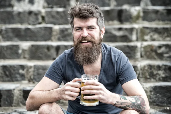 Vrolijke man met bier in zijn handen zittend op stenen trap in het centrum. Glimlachend jongeman met stijlvolle baard ontspannen na het werk. Vrijdag avondje uit, feeststemming — Stockfoto