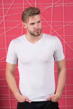 Avrupalı genç bir adam elleri ceplerinde duruyor. Pembe arka planda fotokopi alanı için beyaz tişört giyiyor.