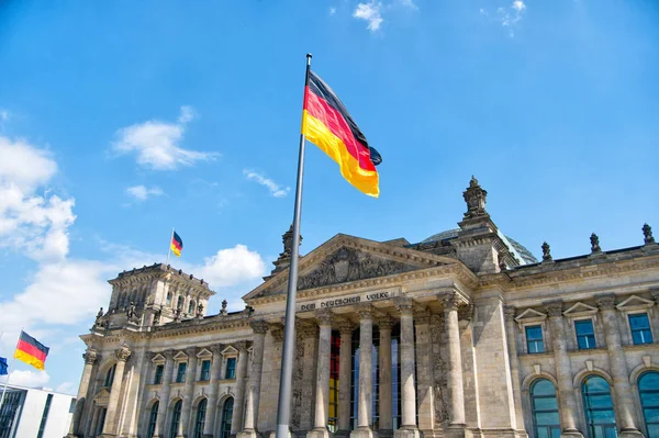 Alman bayrakları, Alman Parlamentosu 'nun (Deutscher Bundestag) ünlü binasında, mavi gökyüzü ve bulutlarla güneşli bir günde, Almanya' nın orta Berlin Mitte bölgesinde rüzgarda sallanıyor. — Stok fotoğraf