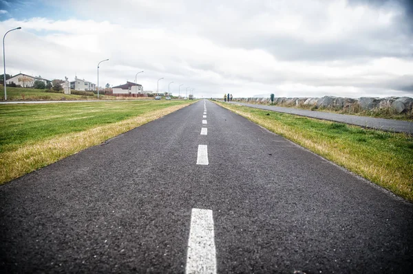 Strada su cielo nuvoloso in reykjavik, ghiandaia. Strada asfaltata con marcatura di superficie con erba sui lati. Viaggio e vagabondaggio. Concetto di libertà o prospettiva e futuro — Foto Stock