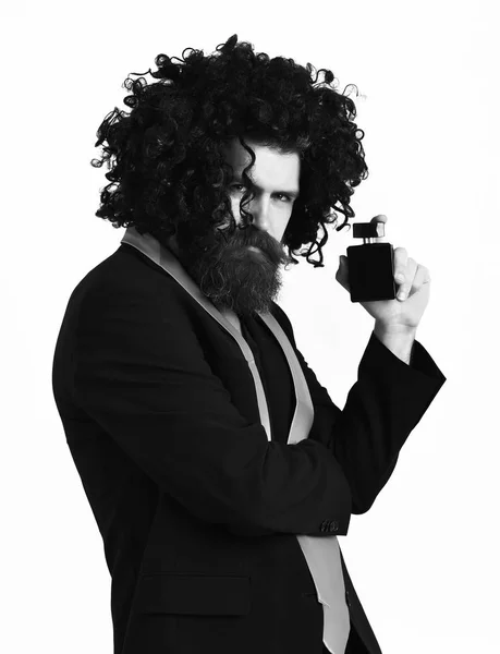 Hipster caucásico en traje y peluca rizada negra sosteniendo perfume —  Fotos de Stock