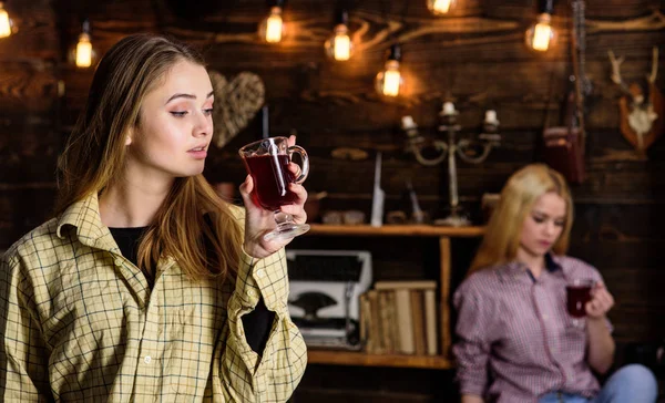 Friends on relaxed faces in plaid clothes relaxing, defocused. Friends enjoy mulled wine in warm atmosphere, wooden interior. Girls relaxing and drinking mulled wine. Rest and relax concept