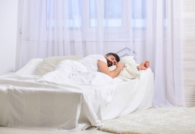Sakin yüz beyaz çarşafımda yatıyor adam, yastık. Adam arka plan üzerinde battaniye, beyaz perdeler ile kaplı yatağa atma. Maço sakal uyku ile rahatlatıcı, nap, sahip rest. NAP ve siesta kavramı