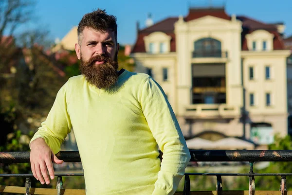 Man with long beard enjoy view from balcony. Relaxation concept. Bearded man have rest on sunny day outdoors. Man with beard and mustache on calm face at balcony, urban background, defocused