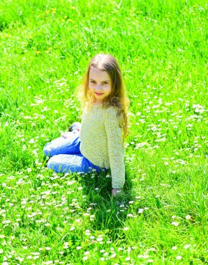 Kız grassplot, arka planı yeşil çimlere oturur. Çocuk çayır otururken bahar güneşli hava keyfini çıkarın. Altın Çağ kavramı. Yüz gülümseyerek kıza harcamak açık havada eğlence
