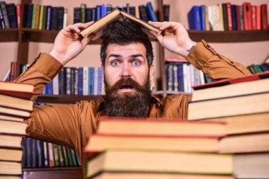 Son tarih kavramı. Öğretmen veya sakallı öğrenci kitabı, defocused çatı yapım masada oturur. Adam Kitaplığı'nda, eğitim sırasında kitaplar, kitap rafı arka plan üzerinde yığınları arasında şok yüzünde