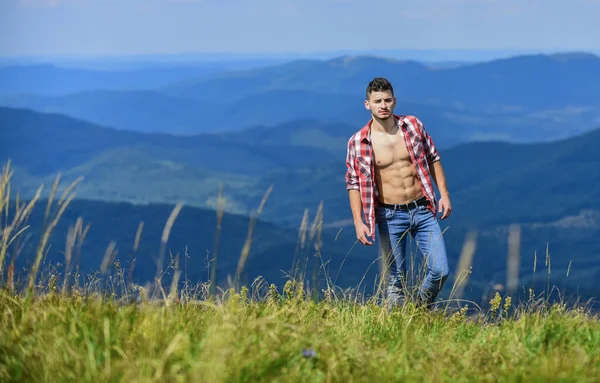 筋肉観光山の丘を歩く。ハイカーの筋肉の胴山のピークに達する。アスリートの男は山をリラックス。美しい環境だ。ハイキングのコンセプト。男は山の風景の背景に立つ — ストック写真