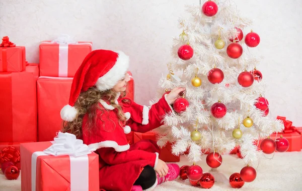 Dzieciak ozdabiający choinkę. Umiłowana wakacyjna aktywność. Dziecko lubi tradycje rodzinne. Koncepcja Wigilii. Dołącz do świętowania Bożego Narodzenia. Dziewczyna uśmiechnięta uroczy Święty Mikołaj siedzieć w pobliżu choinki — Zdjęcie stockowe