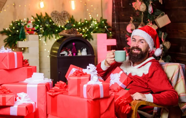 Weihnachten ist die Zeit, um zu gefallen. rotes Weihnachtsmannkostüm. glücklicher Mann trinkt Tee. Milch für Weihnachtsmann. bärtiger Mann mit Geschenkbox. Weihnachtsgeschenke. Weihnachtsgeschäft. Frohe Weihnachten. frohes neues Jahr — Stockfoto
