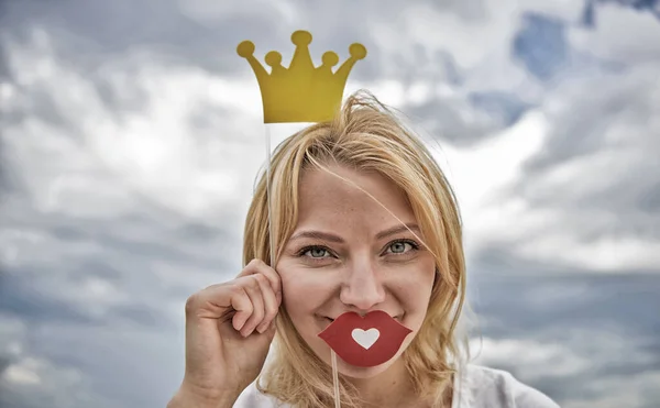 Princesa juguetona. Mujer cabello rubio sostienen tiara de cartón o corona y labios rojos símbolo del amor fondo del cielo. Sueña con que cada chica se convierta en reina. Lady princesa posando alegre con corona amarilla — Foto de Stock