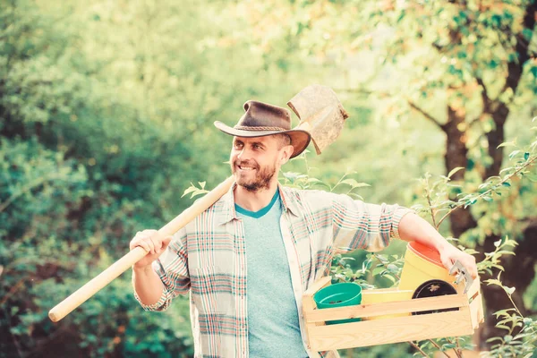 Muskulös ranchman i cowboyhatt. Eko-lantarbetare. Skörda. Glad jorddag. Ekologiskt liv. jordbruk och jordbruk. Trädgårdsutrustning. sexig bonde hålla spade och box med pott. Göra ditt liv färgat — Stockfoto