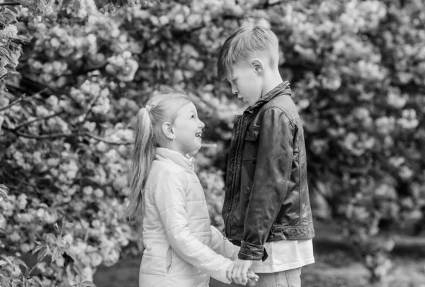 Pembe kiraz çiçeğine aşık çocuklar. Havada aşk var. Çift sevimli sevimli çocuklar sakura bahçe yürümek. Şefkatli aşk duyguları. Küçük kız ve oğlan. Parkta romantik bir randevu. Aşık olmak için bahar zamanı