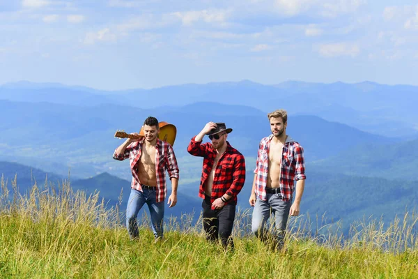 Tipos amigáveis com caminhadas de guitarra no dia ensolarado. Conceito de caminhadas de turistas. Aproveitando a liberdade juntos. Grupo de jovens em camisas quadriculadas caminhando juntos no topo da montanha. Caminhadas com amigos — Fotografia de Stock