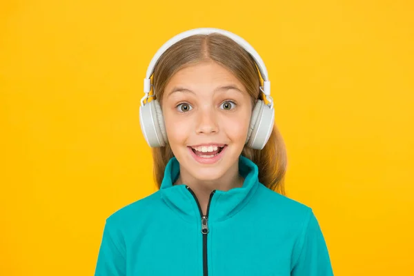 A canção feliz faz-lhe sorrir. Menina pequena feliz ouvir música no fundo amarelo. Criança gosta de cantar em fones de ouvido. Sorri na cara feliz. A música tem emoções felizes — Fotografia de Stock