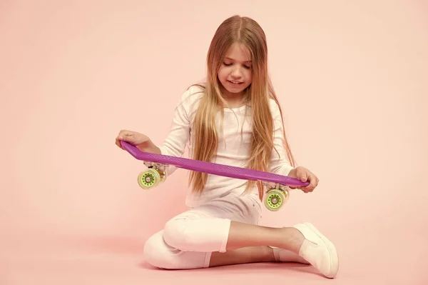 スケーターの女の子やスケートボーダー。ピンクの背景にスケートボードを持つ小さな女の子。バイオレットペニーボードを持つかわいい小さな女の子。スケーターの女の子のスタイルと外観を持つ愛らしい子供 — ストック写真