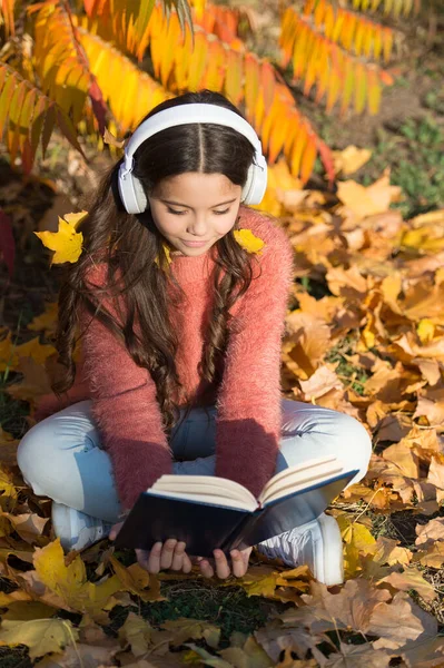 Opportunities for audio learning. Cute kid in stereo earphones sit on autumn leaves. Little child enjoy audio learning. Small girl listen to audio book in headphones. Audio materials for lesson