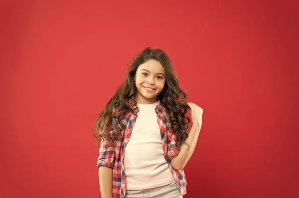 Casual but amazing look. Adorable girl with fashion look on red background. Cute little child having glamour look of long curly hairstyle. Vogue look of small fashion model