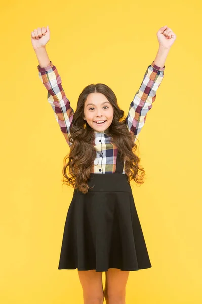 Celebrate the childhood. Happy girl with raised hands yellow background. Small girl back to school. Girl celebrating school holidays. Cute girl with long hair smile in formal wear — Stock Photo, Image