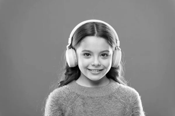 Muzyka daje przyjemność. Perfekcyjne słuchawki stereofoniczne. Dziewczyna cute little dziecko nosić słuchawki słuchać muzyki. Dziecko słuchać muzyki pomarańczowe tło. Zalecana muzyka na podstawie początkowego zainteresowania — Zdjęcie stockowe