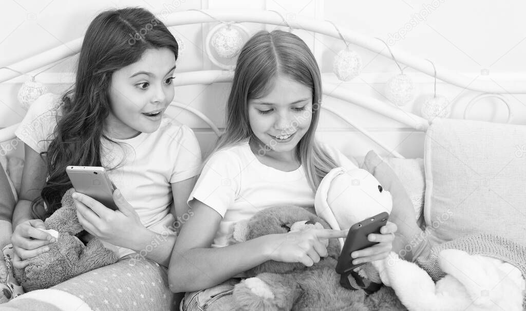 It cant be true. Happy little children with mobile phone. Merry Christmas and Happy New Year greetings. Little girls use smartphone in bed. Ordering gifts for Christmas and New Year by phone