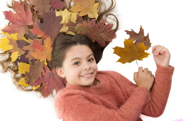 Prevent dry split hair ends. Child enjoy fall season. Girl cute kid long hair lay on white background with fallen leaves. Dry maple leaves in hairstyle. Fall season concept. Hair care in autumn