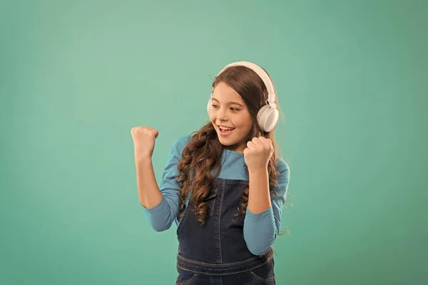 No es más que una ganadora. Niño feliz haciendo gesto ganador sobre fondo azul. Pequeño ganador escuchando música en auriculares. Emocionado ganador o campeón celebrando la victoria — Foto de Stock