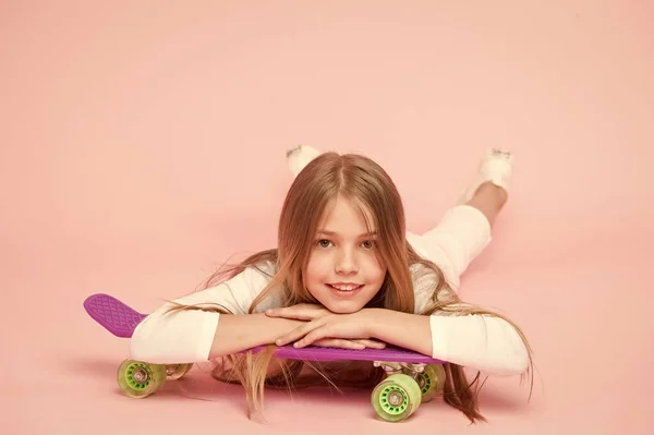 O skate criou o hipster. Adorável pequeno patinador sorrindo com estilo hipster e olhar. Pequeno hipster bonito relaxante no skate em fundo rosa. hipster feliz com placa de moeda violeta — Fotografia de Stock