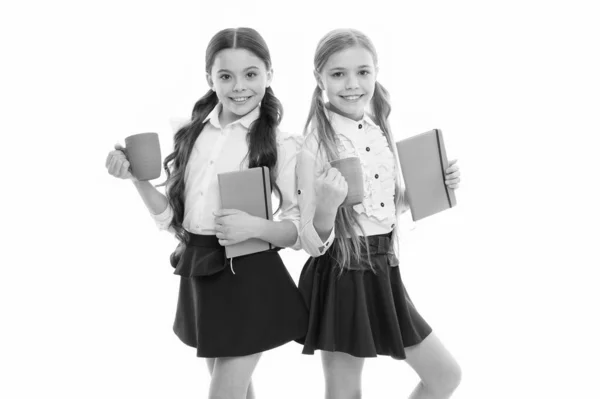 В обеденный перерыв. Милые школьницы с чашками и книгами. Маленькие девочки наслаждаются школьным обедом. Маленькие дети пьют чай или молоко на обед. Школьные дети обедают — стоковое фото