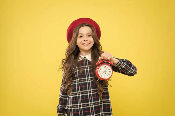 Çalar saatini takıyor. Mutlu küçük kız sarı arka planda çalar saat tutan. Mekanik saatle gülümseyen küçük çocuk. Uyandırma saati — Stok fotoğraf