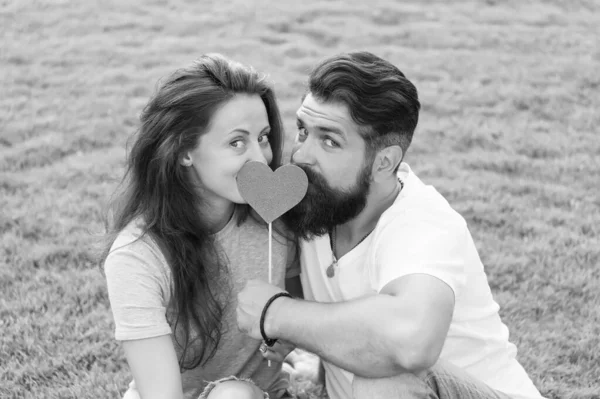 Le dio su corazón. Pareja sensual enamorada del corazón de utilería sobre hierba verde. Mujer sexy y hombre barbudo sosteniendo el corazón de San Valentín en palo. Un corazón dos almas — Foto de Stock