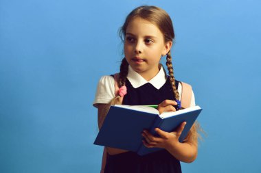 Kız büyük mavi bir defterle yazıyor. Okul üniformalı bir öğrenci.