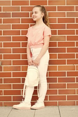 Tepeden tırnağa şık. Şık bir görünüme sahip küçük bir model. Şık moda giyim uzun sarı saçlı küçük sevimli çocuk. Kırmızı tuğla duvarda sevimli şık kız