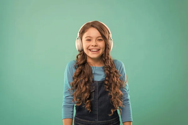 Jogue o momento. Miúdo giro a ouvir música nos auscultadores estéreo. Adorável usuário fone de ouvido no fundo azul. Criança pequena usando fone de ouvido branco ajustável. Menina usando fone de ouvido sem fio — Fotografia de Stock