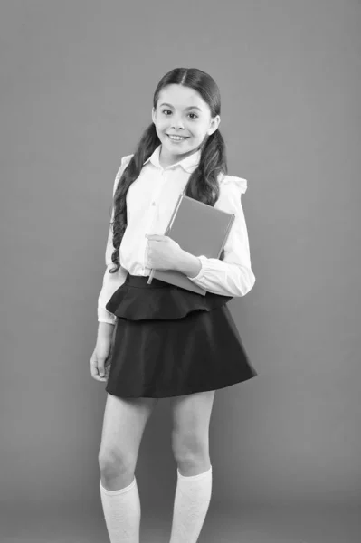 Torniamo a scuola. Emozionata dalla conoscenza. diario per prendere appunti. ottenere informazioni libro modulo. piccola ragazza in uniforme scolastica. scolaretta che scrive appunti su sfondo arancione. curriculum scolastico — Foto Stock