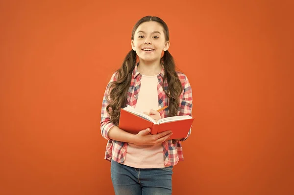 Investiga la lectura. Lindo niño pequeño leyendo un libro sobre fondo naranja. Adorable niña aprender a leer y escribir. Lectura y escolarización en el hogar — Foto de Stock