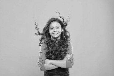 Mutlu ve nefes kesici görünüyorsun. Mavi arka planda uzun kıvırcık saçlı mutlu küçük kız. Modayla gülümseyen neşeli küçük bir çocuk. Sevimli çocuk mutlu bir çocukluk geçiriyor