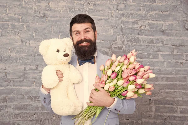Romantic gift. Macho getting ready romantic date. Man wear blue tuxedo bow tie hold flowers bouquet. International womens day. Surprise will melt her heart. Romantic man with flowers and teddy bear
