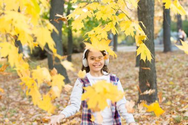 Yapraklar düştüğünde. Küçük kız müzik dinlerken yapraklarla oynuyor. Mutlu çocuk sonbahar yapraklarıyla iyi eğlenceler. Yapraklar sonbaharda renk değiştirir