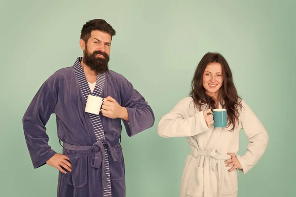 Chaque matin commence par un café. Couple en peignoirs avec des tasses. Homme barbu et femme endormie dégustent du café ou du thé le matin. Le type en tenue de bain tient du thé café. Commencez une nouvelle journée. Concept petit déjeuner — Photo