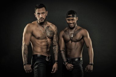 Seksi torsolar siyah arka plan üzerine izole ile moda modelleri. Sporcular giyen karanlık kot pantolon ve moda aksesuarları, sağlık ve fitness kavramı büyük kaslı. Arkadaş grubu dövmeler birlikte poz