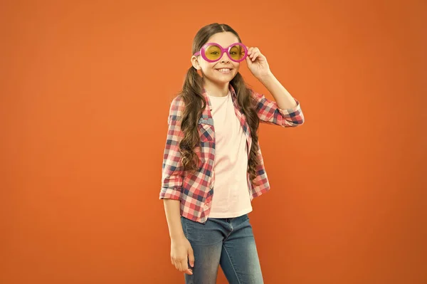 Γυαλιά τέλεια για το στυλ της. Μικρό παιδί που φαίνεται χαρούμενο στα γυαλιά μόδας. Μικρό παιδί χαμογελά με γυαλιά πάρτι σε πορτοκαλί φόντο. Αστείο κορίτσι φορώντας γυαλιά ηλίου με φίλτρο χρώματος — Φωτογραφία Αρχείου