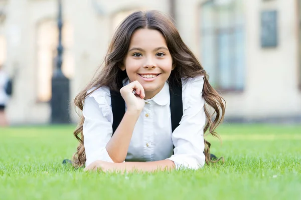 Child back to school and looking cool. Happy small child relax on green grass. Little child smiling with long brunette hair. Cheerful female child in formal school uniform outdoor — 스톡 사진