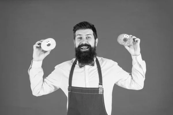 Sie teilen lustige Donuts. bärtiger Mann mit Ring-Donuts auf rotem Hintergrund. Profi-Bäcker mit leckeren glasierten Donuts. Hipster mit gebratenen Donuts in der Hand — Stockfoto