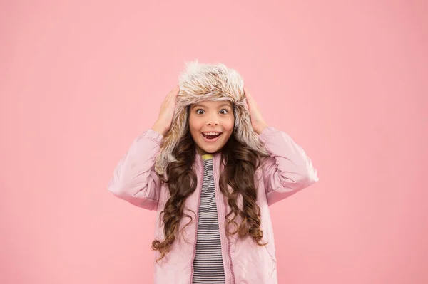 Wintervakantie. Jeugdactiviteit. warme kleding voor het koude seizoen. Verrast kind roze achtergrond. Kindermode. trendy meisje ziet eruit als hipster. bont oorflap hoed accessoire. klein meisje winter hoed — Stockfoto