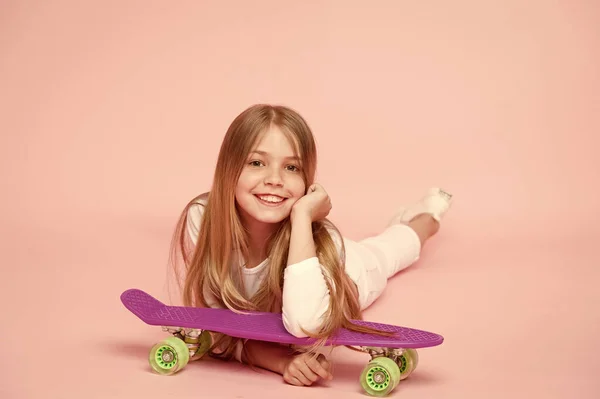 Niño adorable niño pelo largo adoro paseo penny board. Feliz infancia. Montar tablero de peniques y hacer trucos. A la chica le gusta andar en monopatín. Estilo de vida activo. Chica divirtiéndose con penny board fondo rosa — Foto de Stock