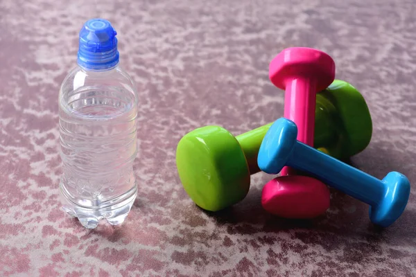 Dumbbells made of plastic near water bottle on burgundy background