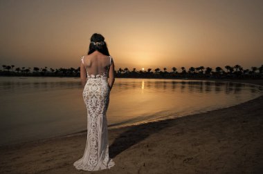 Gelin beyaz gelinlik kumlu plajda standı. Gelinlik. Gelin mutlu gün batımı okyanus arka plan keyfini çıkarın. Akşam seremonisi. Deniz tatil beldesinde balayı. Yurt dışında düğün. Düğün töreni deniz kıyısı